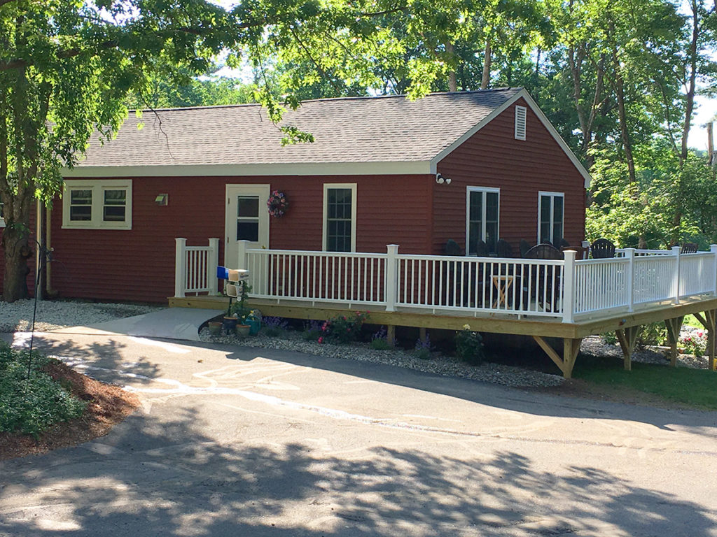 View of Pine Hill retirement home from the driveway circular. It is brick red and has white trim, plus a pressure treated deck with white rails.