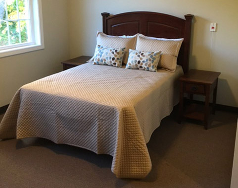 A wooden bed made with a mauve bedspread and decorative pillows