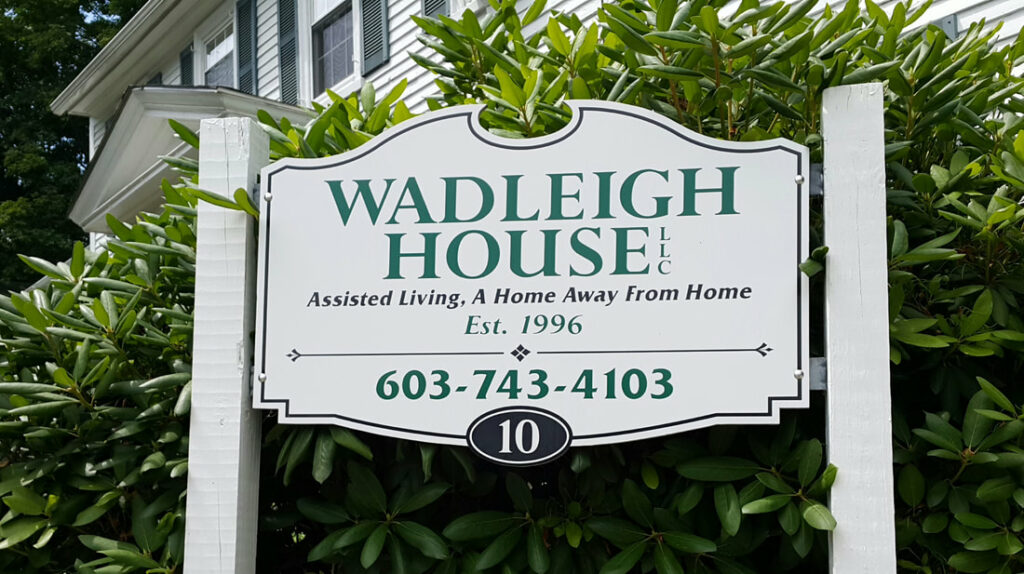 A sign for Wadleigh House with a large rhododendron behind it