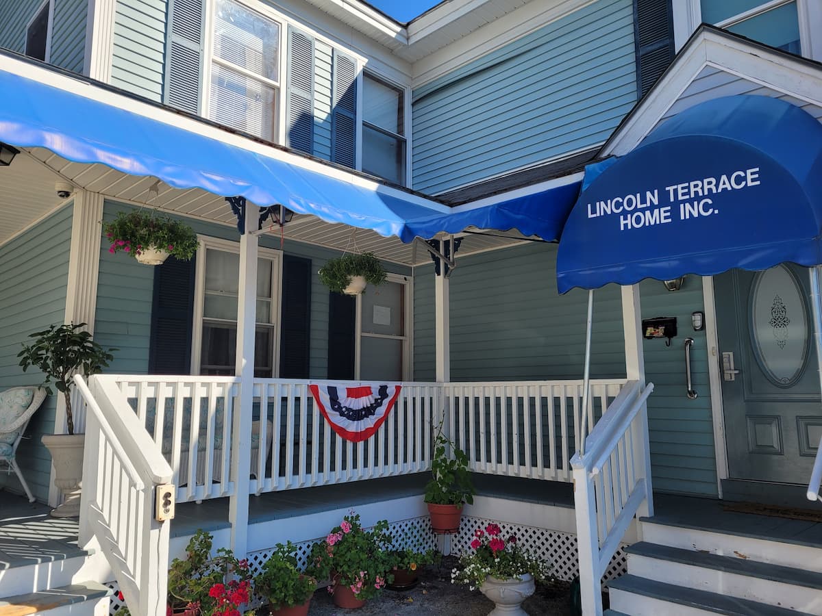 The entry area of Lincoln terrace, a blue building with white trim and dark blue shutters; there are steps up to the porch, which is covered by blue awnings.