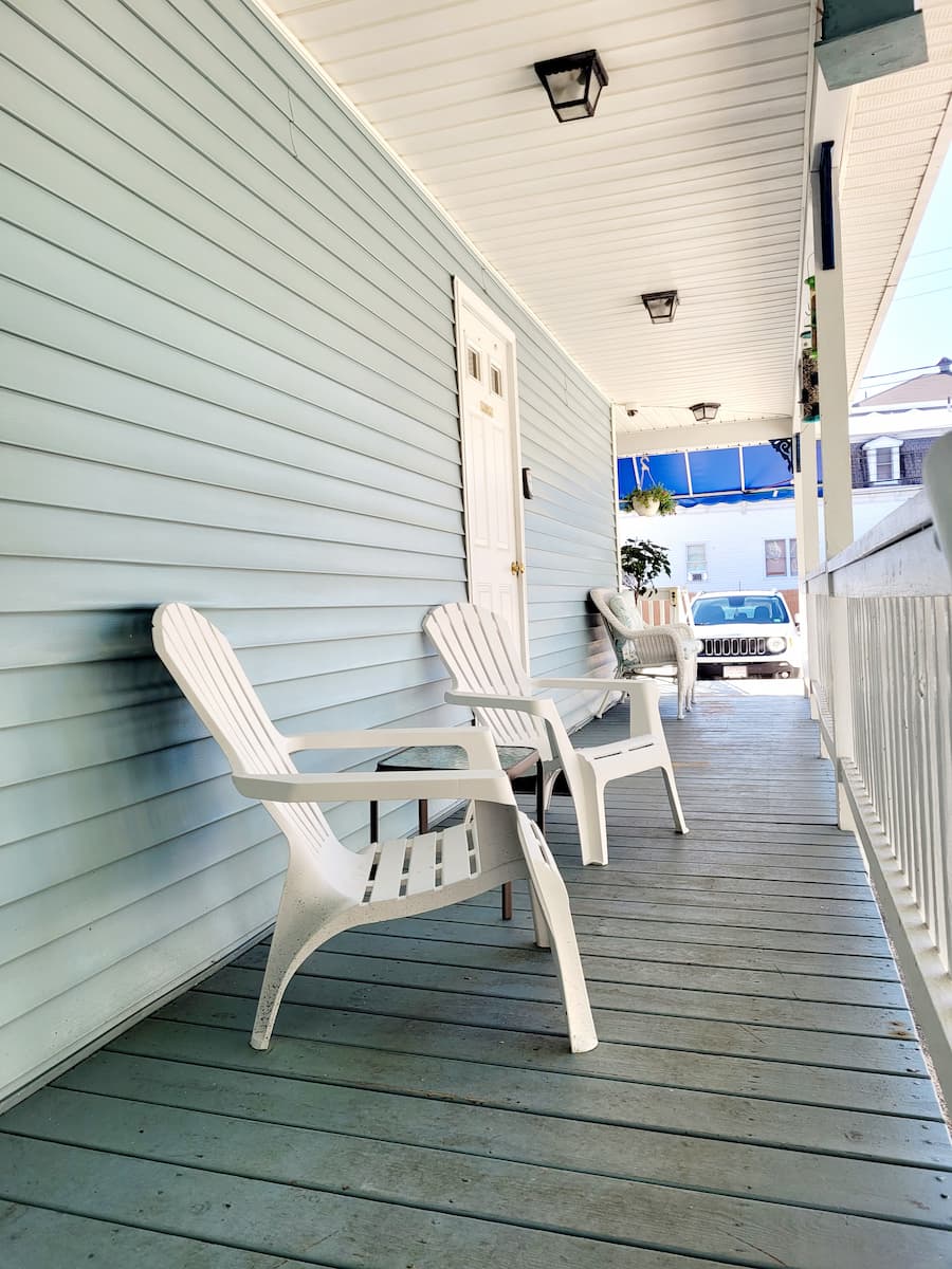The covered porch area of Lincoln Terrace, showing the blue siding and white trim of the house and several white patio chairs.