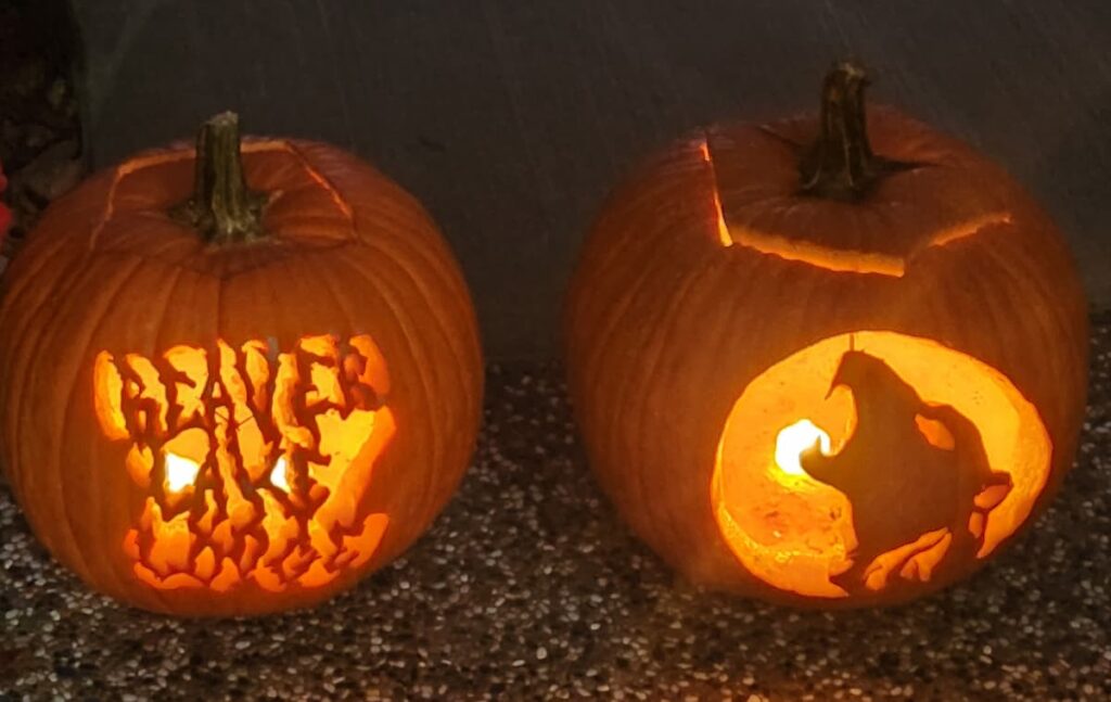 Two carved pumpkins side-by-side. The first pumpkin says "Beaver Lake Lodge" where the second is of a howling wolf.