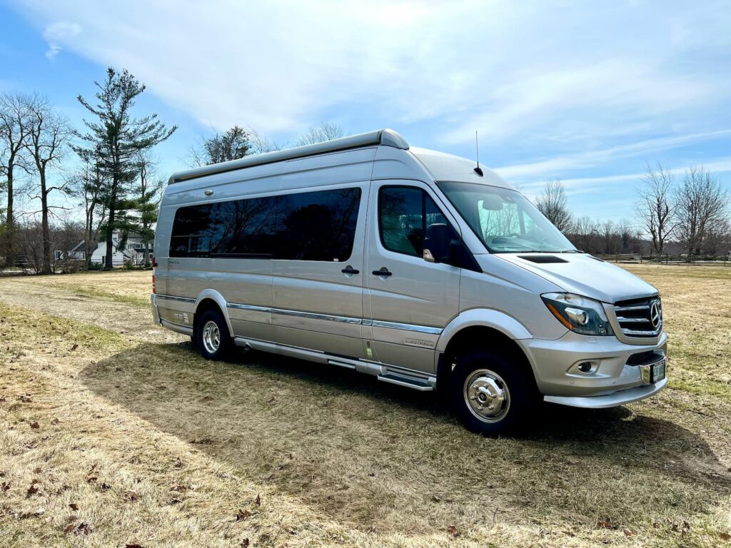 Van A silver airstream van parked in a grassy lot.